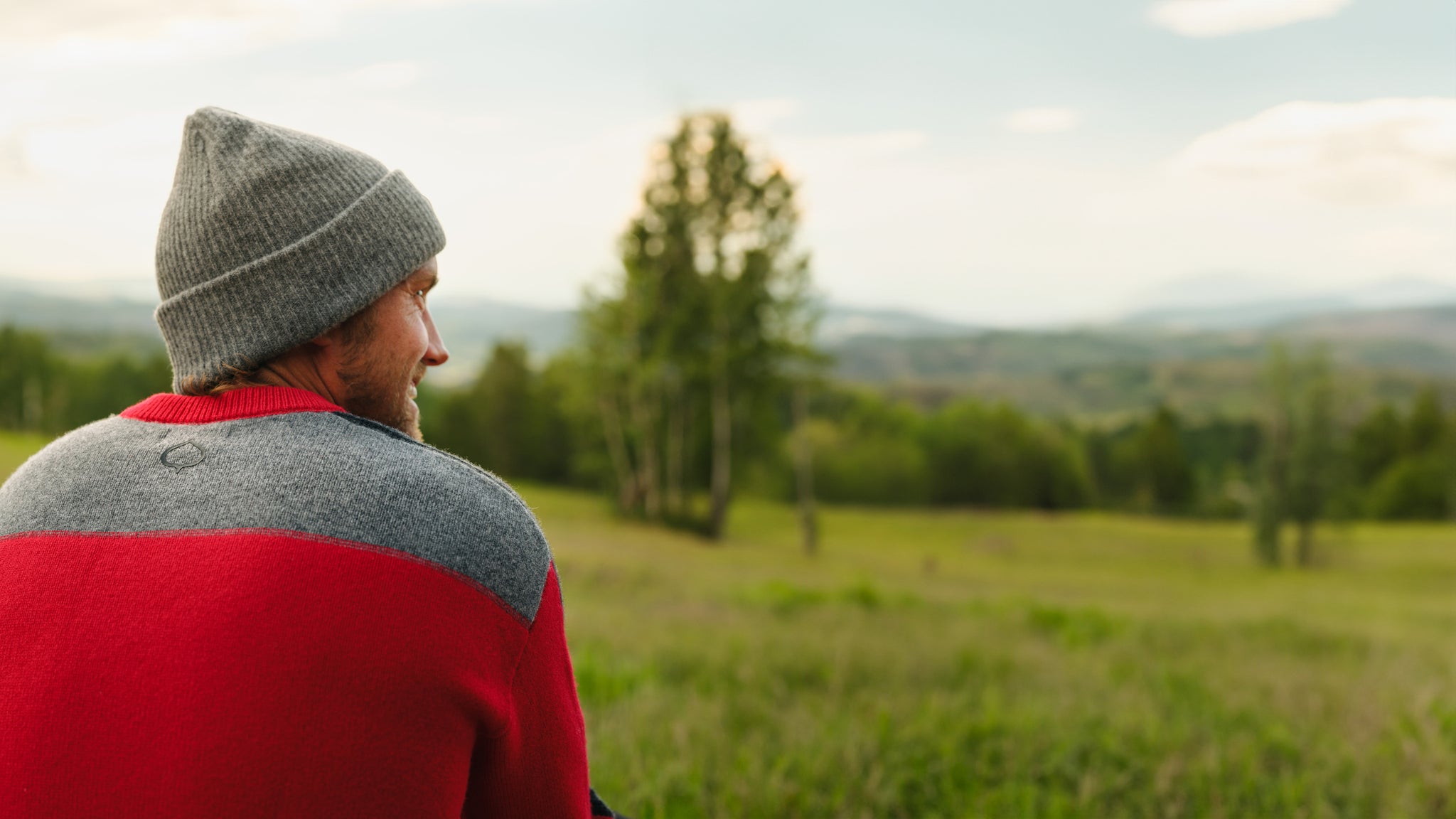 Man wearing ASPENX sweater and beanie in a field with trees.